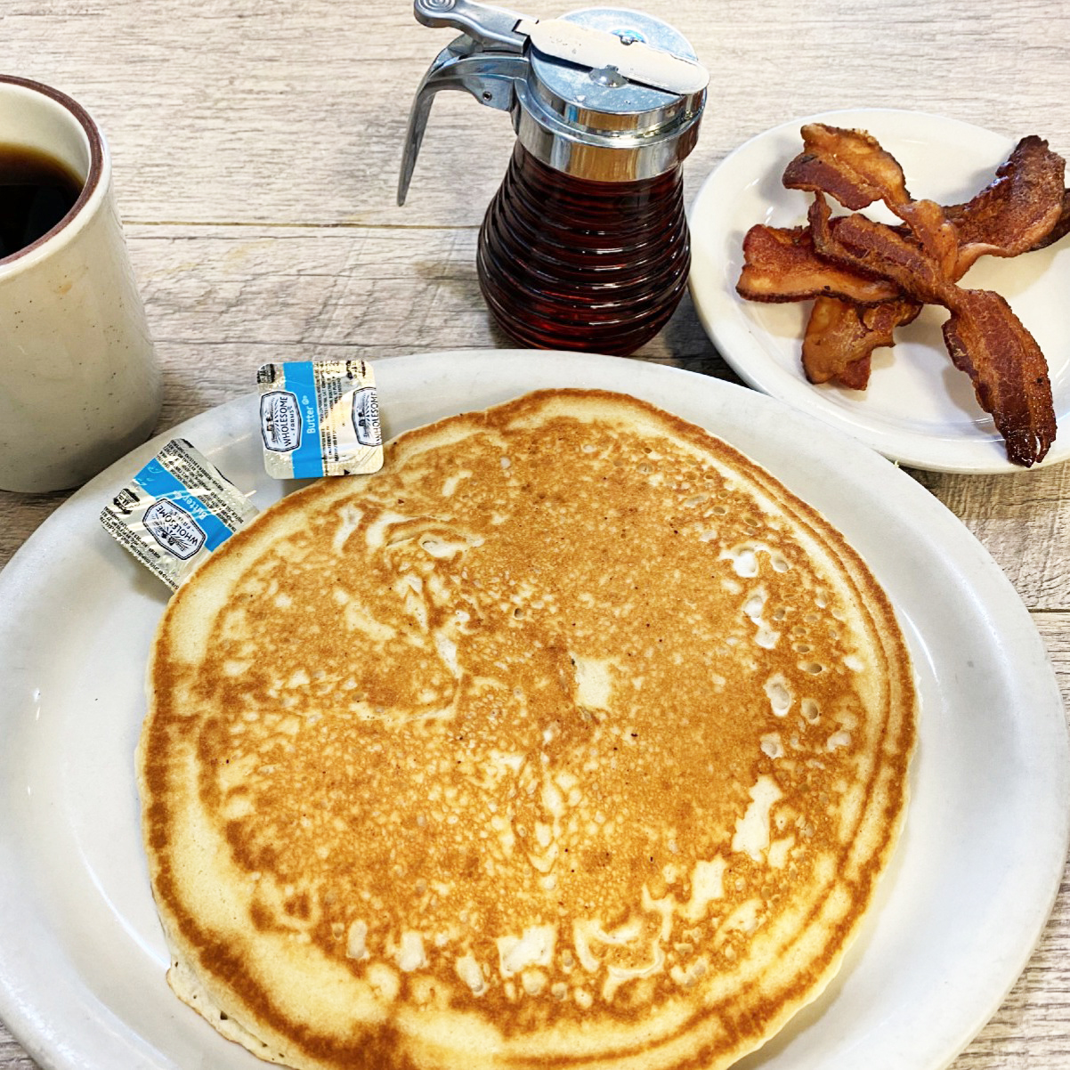 pancakes, next to bacon, syrup and coffee